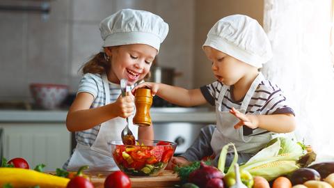 Zwei Kinder mit Kochmützen kochen in einer Küche. 