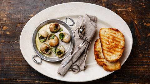 Schnecken mit Kräuterbutter und geröstetem Brot sauf einem Teller. 