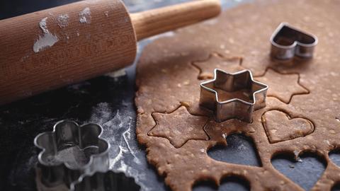 Aus Teig werden auf dunklem Untergrund weihnachtliche Motive für Lebkuchen ausgestochen.