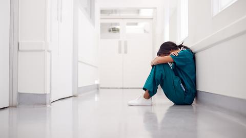 Eine Ärztin kauert erschöpft am Boden eines Krankenhauses. 
