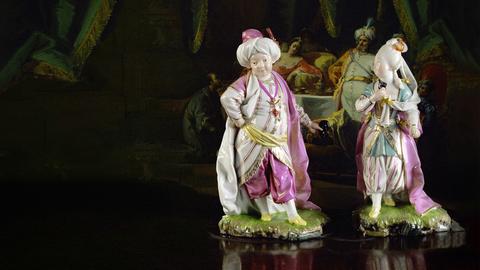 Zwei Porzellanfiguren vor einem Gemälde. Text: Die Höchster Porzellan-Geschichte – weißes Gold vom Main