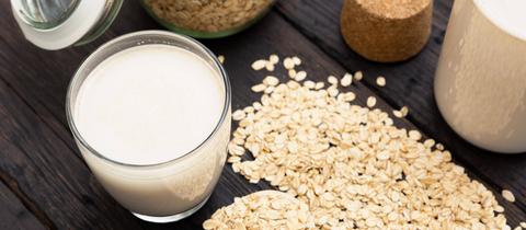 Glass of vegan, dairy-free oat milk and oats on a dark wooden background with texture. 