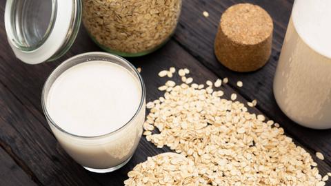 Glass of vegan, dairy-free oat milk and oats on a dark wooden background with texture. 