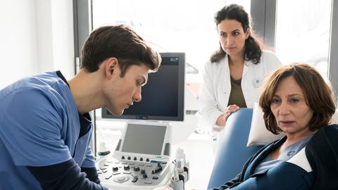 Es gibt einen Neuzugang am Johannes-Thal-Klinikum: Assistenzarzt Florian Osterwald (Lion Wasczyk, l.) darf, unter der Aufsicht von Leyla Sherbaz (Sanam Afrashteh, h.) seine erste Patientin untersuchen.