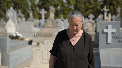 Eine ältere Frau steht auf einem Friedhof zwischen Gräbern