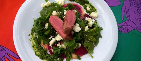 Hauptgang von Carina Jakisch. Lammlachse auf Rote-Bete-Apfle-Carpaccio mit Grüne Soße Pesto auf einem weißen Teller.