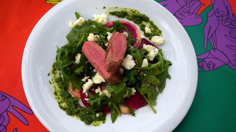 Hauptgang von Carina Jakisch. Lammlachse auf Rote-Bete-Apfle-Carpaccio mit Grüne Soße Pesto auf einem weißen Teller.