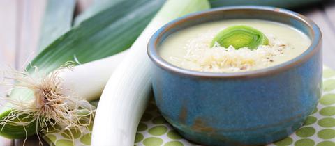 Lauchsuppe in einer Schüssel. Zwei Stangen Lauch liegen daneben.