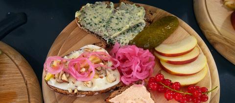 Hessische Brotzeitplatte von Carina Jakisch. Drei belegte Brote, Apfelschnitze und Johannisbeeren auf einem runden Holzbrett.