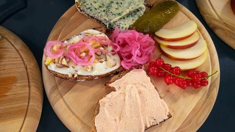 Hessische Brotzeitplatte von Carina Jakisch. Drei belegte Brote, Apfelschnitze und Johannisbeeren auf einem runden Holzbrett.