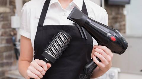 Eien Friseurin hält Föhn und Bürste.