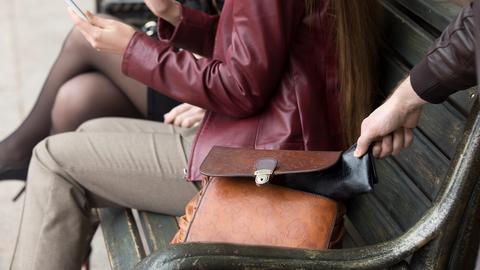 Ein Taschendieb greift nach einem Portemonnaie in einer Tasche.