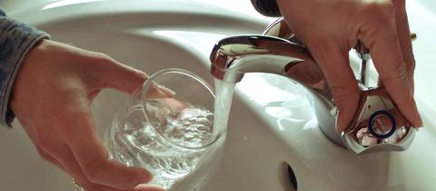 Jemand hält ein Glas unter einen fließenden Wasserhahn.
