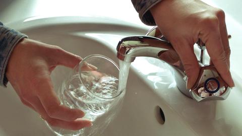 Jemand hält ein Glas unter einen fließenden Wasserhahn.