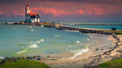 Ein Leuchtturmhäuschen am Meer bei rosa Himmel. Text: Entspannen in Nordholland