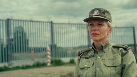 Die polnische Grenzschützerin Katarzyna Zdanowicz in Uniform vor einem Grenzzaun mit Stacheldraht.