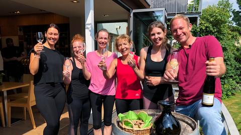 Tobi und Frauen stoßen bei der Weinprobe lachend an. 