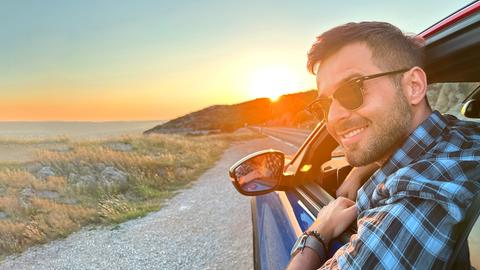 Reporter Danijel Stanic sitzt in einem Oldtimer-Auto und fährt an der Küste Kroatiens der Abendsonne entgegen.