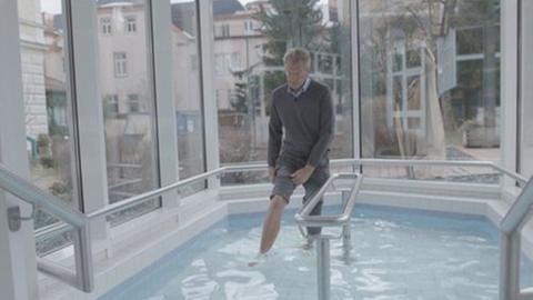 Mann steht mit hochgekrempelter Hose in einem Indoor-Pool. 