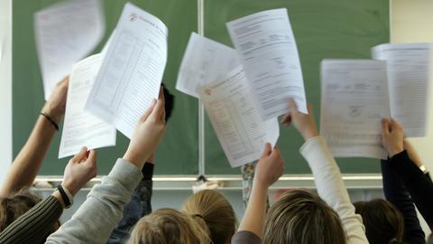 Schüler*innen halten vor der Tafel ihre Halbjahreszeugnisse nach oben in die Luft.