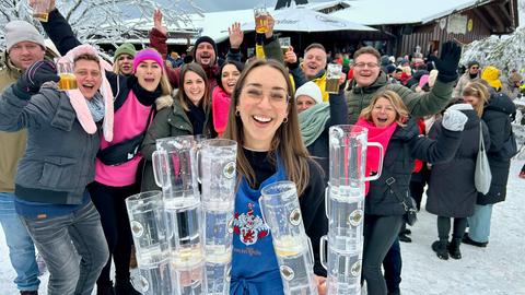 7-Tage-Reporterin Isabell Kramer hält leere Bierkrüge in den Händen. Hinter ihr im Schnee feiernde Urlauber beim Après-Ski.
