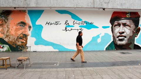 Hugo Chavez läuft vor einer Mauer mit einem Bild von Fidel Castro.