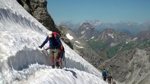 Bergsteiger durchqueren ein Schneefeld auf dem Heilbronner Weg.