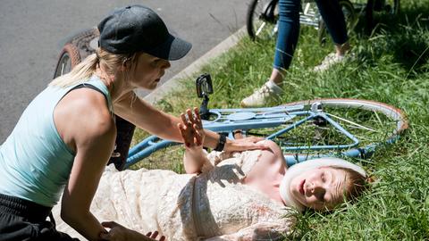 Eine Frau kümmert sich um eine vom Fahrrad gestürzte Frau im Brautkleid.