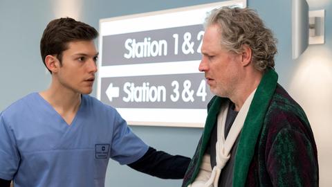 Ein junger Arzthelfer berihigt einen älteren Mann mit Armgips