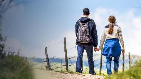 Ein junges Pärchen steht Hand in Hand auf einem Feldweg.