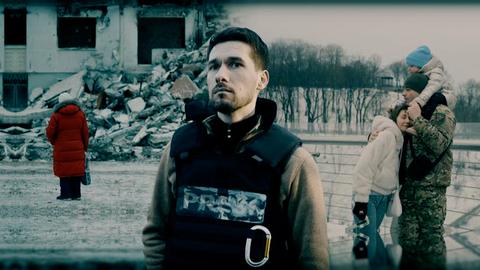 Ein Mann in schusssicherer Weste steht zwischen den Trümmern in der Ukraine