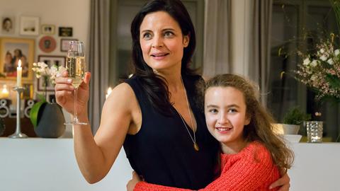 Susanne Mertens (Elisabeth Lanz, l.) begrüßt mit Pflegetochter Luisa (Deborah Mary Schneidermann, r.) im Arm die Gäste auf der Einweihungsparty ihrer neuen Wohnung.