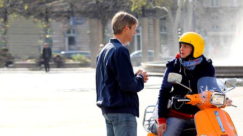Hanna (Jördis Triebel) und Andi (Andreas Schmidt) begegnen sich vor einem großen Springbrunnen. Sie sitzt auf einer Vespa.