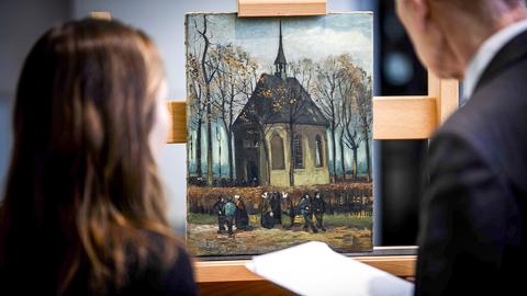 Im Mittelpunkt ist das Gemälde “Die Kirche von Nuenen mit Kirchgängern” von Van Gogh zu sehen, davor stehen zwei Personen und betrachten das Bild.