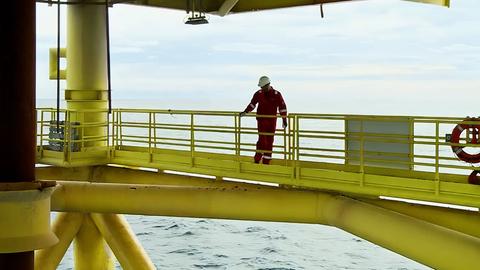 Ein Mitarbeiter steht auf einer Ebene der Bohrinsel und schaut hinunter aufs Meer.