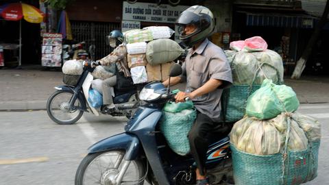 Schwer beladene Mopedfahrer im Straßenverkehr von Hanoi.