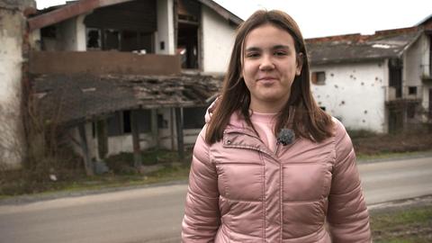 Tamara steht vor einem Haus. 