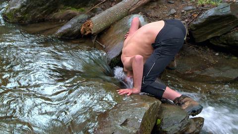 Protagonist wäscht sich Kopf und Haare in einem Fluss.