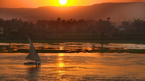 Ein Segelboot fährt im Sonnenuntergang über den Nil.