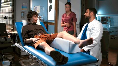 Ein Arzt untersucht einen jungen Mann am linken Bein.