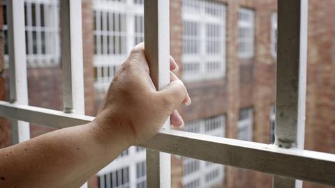 Blick aus dem Gitterfenster der Jugendstrafanstalt Ploetzensee. Eine Hand hält sich am Gitter fest.