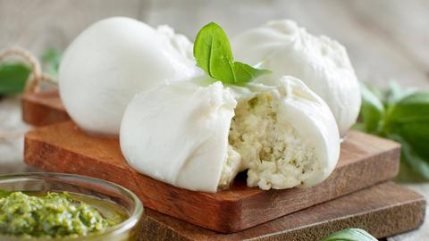 Drei Kugeln Mozzarella auf einem Holzbrett. Die vordere Kugel ist angeschnitten: der Mozzarella ist mit Ricotta gefüllt.