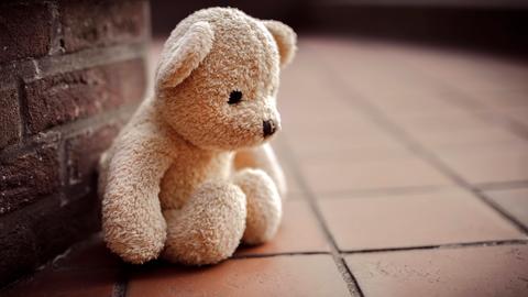 Ein Teddybär sitzt an eine Steinwand gelehnt auf einem Steinboden.
