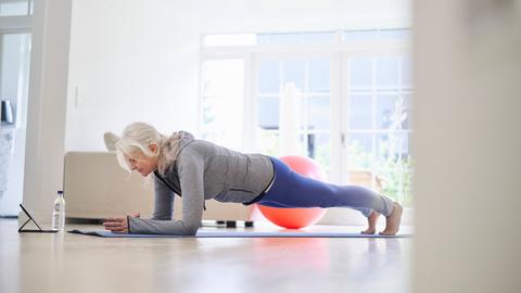 Eine ältere Frau in der Plank-Position auf dem Boden ihres Wohnzimmers.