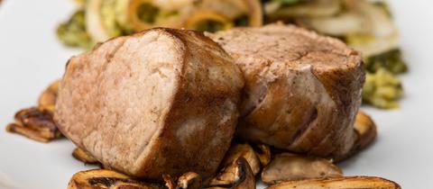 Zwei Stück Schweinefilet auf einem Teller, im Vordergrund kleingeschnittene Pilze.