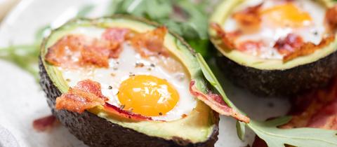 Die Hälfte einer überbackenen Avocado mit Ei und Speck.