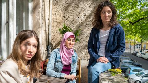 Drei junge frauen sitzen bei sommerlichen Wetter auf einem Balkon. Die mittlere trägt ein Kopftuch.
