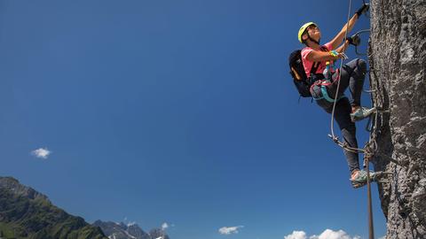 Eine Frau klettert gesichert an einem Berg hoch. Text: Mindelheimer Klettersteig.