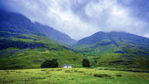 Graue Wolken über Glen Coe. Ein einziges Haus steht am Fuß des Berges.