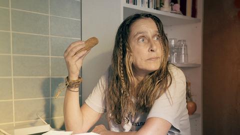 Eine Frau sitzt in der Küche und isst etwas aus der Hand.